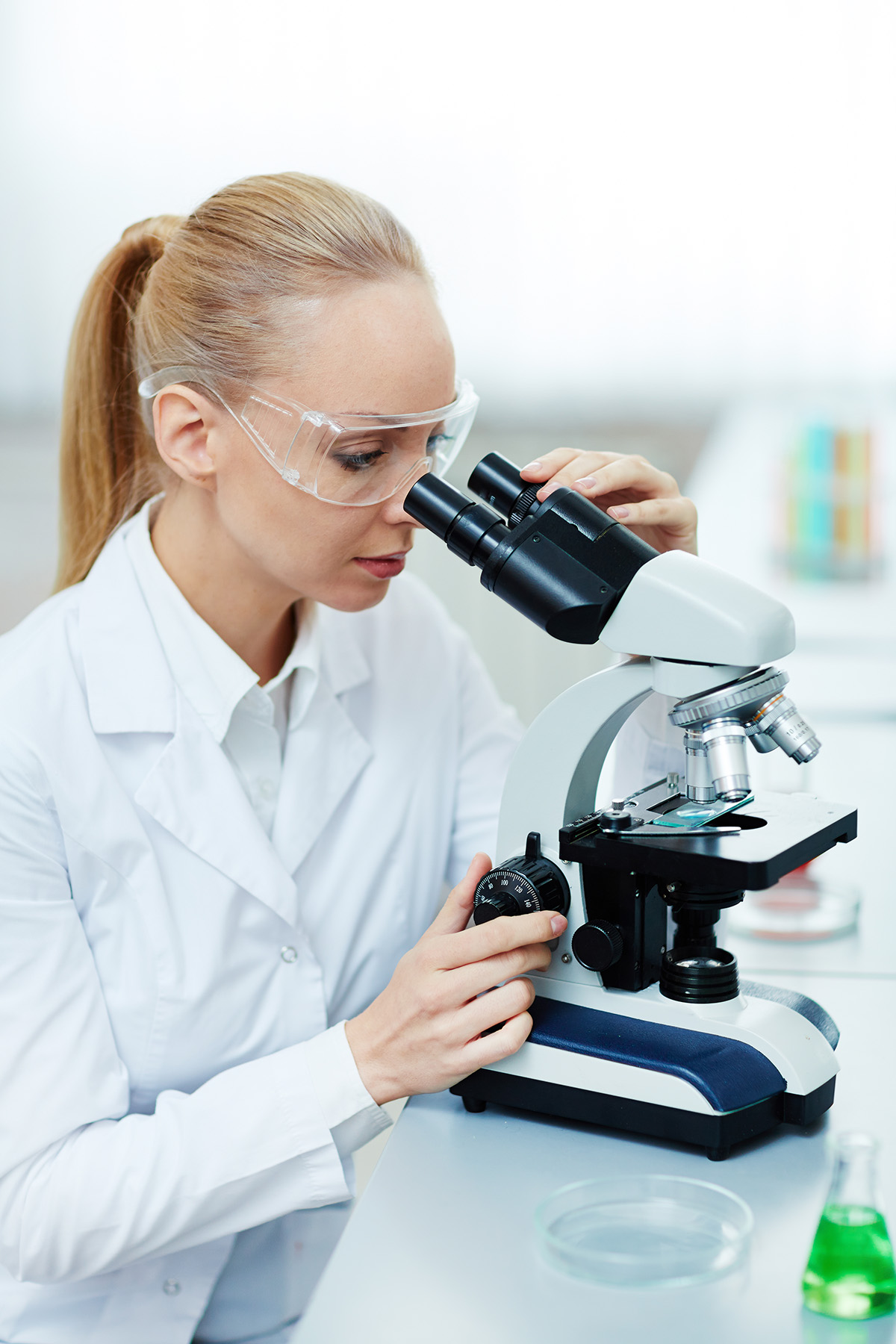Young woman in whitecoat looking in microscope